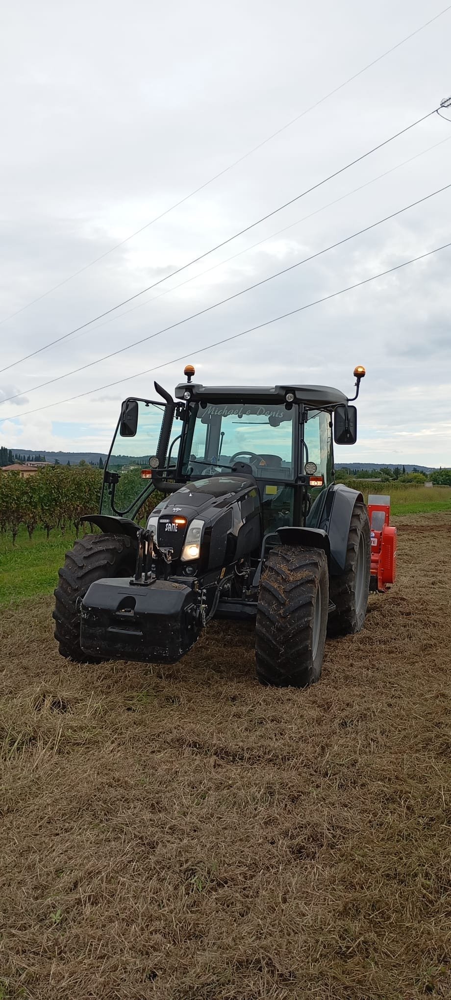 Black and red farm tractor parked in a field with power lines and agricultural landscape in background